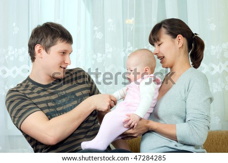happy family home: father, mother and baby sitting against the window