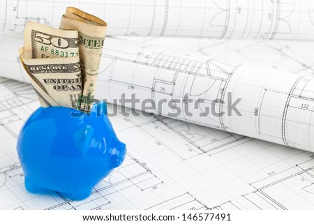 Blue piggybank with dollar bills on home construction plans - home building financing concept
