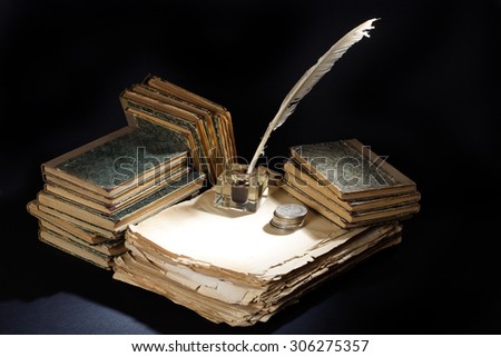 Old fountain pen, books and inkwell and silver coins on a black textured background