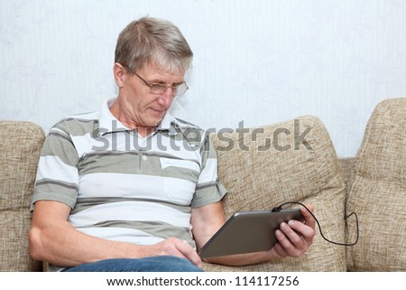Senior adult Caucasian man interested with a new tablet computer, sitting on sofa in domestic room