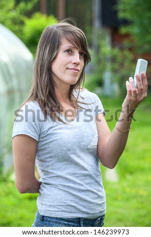 Thoughtful young woman standing at nature and holding cell phone up for good connection