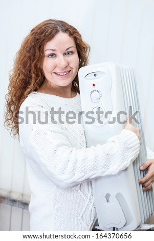 Happy Caucasian young woman embracing new oil heater in domestic room