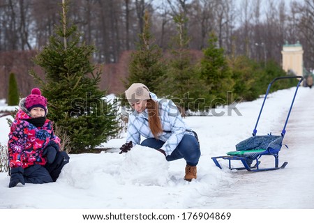 Mother helping her daughter to make a snowman in street