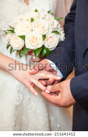 Groom wearing wedding ring on finger of bride, close-up