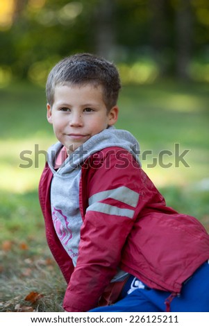 Portrait of young boy in red jacket laying on grass