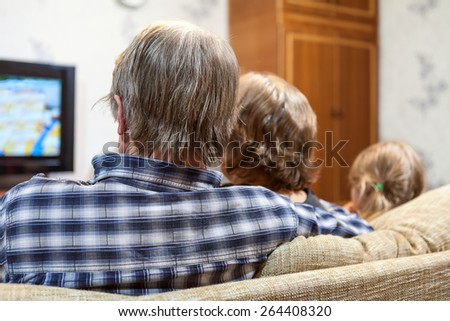 Caucasian family from three people sitting on the sofa together and watching tv, rear view