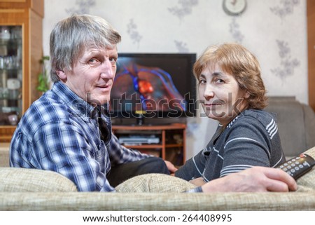 Middle-aged man and woman sitting in front of TV turning back on couch