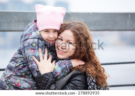 Caucasian mother embracing daughter while walking street, head and shoulders portrait