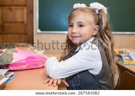 First-form schoolgirl in uniform sitting clasped hands at school desk, side view