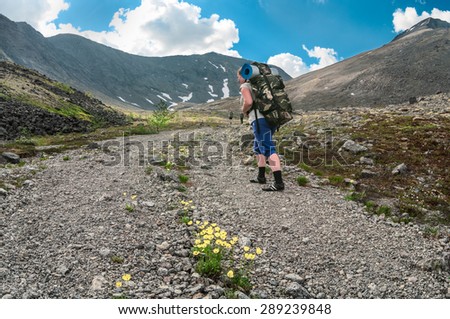 Woman hiker with backpack follows the main group climbing the mountain road