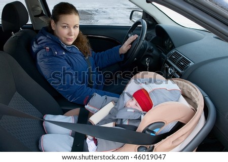 The child in a safety seat near to mother who sits on forward sitting of the car. Child not in focus