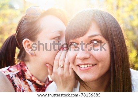 Young beautiful woman whispers something to girlfriend