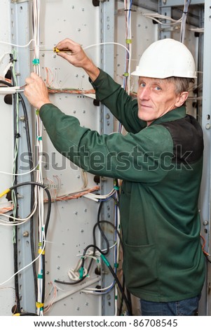 Mature male electrician working in hardhat with cables and wires, looking at camera