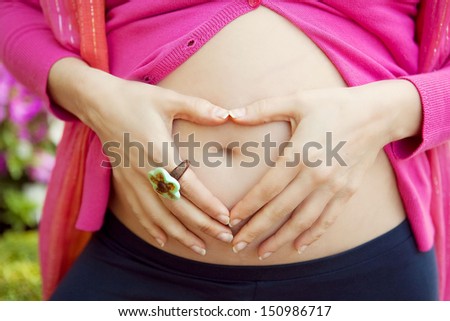 woman hand with heart shape in her pregnant belly