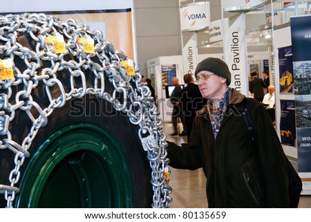 MOSCOW - APRIL 13: Man looks at the tire with chain at the international exhibition of  the Mining and Processing of Metals and Minerals, MiningWorld on April 13, 2011 in Moscow
