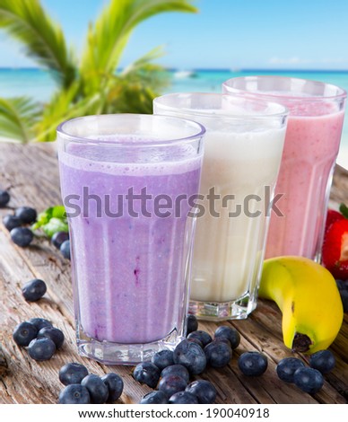 Fresh milk, strawberry, blueberry and banana drinks on wodeen table with tropical beach, assorted protein cocktails, fruits.
