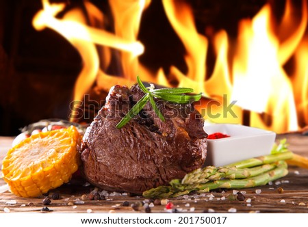 Grilled fresh Beef Steak with flames. Delicious beef steaks with fresh vegetable and trimmings on wooden table.
