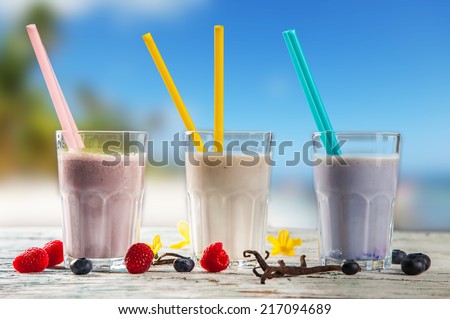 Fresh milk, raspberry, blueberry and vanilla drinks on wooden table, assorted protein cocktails with fresh fruits and nature background. Healthy lifestyle.
