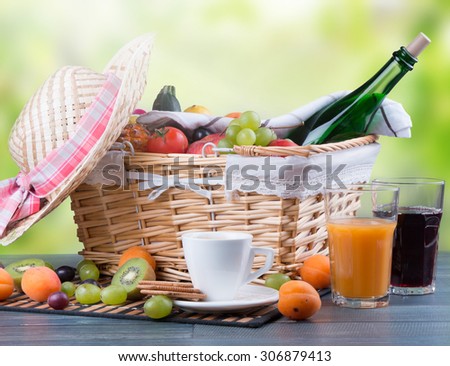 Summer picnic on wooden table with a basket of food, nature green background