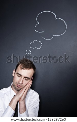 sleeping businessman with a thought cloud on the blackboard wall behind him