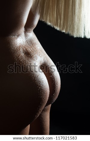 Beautiful rear view of a nude young woman with long blond hair and wet body in front of black background