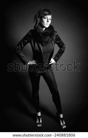 Full length monochrome portrait of a beautiful young woman with read hair wearing black blazer and fur in front of dark studio background
