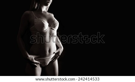 Wet body of a blond young woman in beautiful white underwear in front of black background, monochrome photo with copy space on the right side of the image
