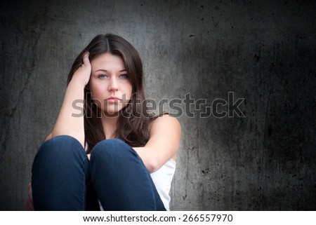 Outdoor portrait of a sad teenage girl looking thoughtful about troubles in front of a gray wall, photo with copy space on the right side of the image