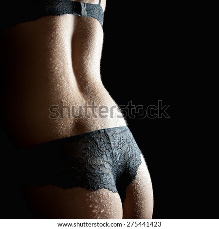 Beautiful back of a woman wearing undies and bra in front of black studio background, closeup photo