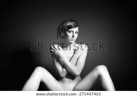 Monochrome fashion portrait of a beautiful nude woman in front of dark background, her private parts are not visible