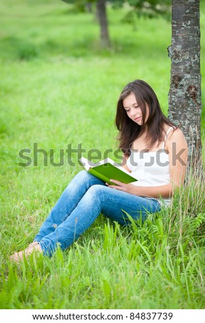 Outdoor portrait of a cute teen sitting under a tree and reading a book