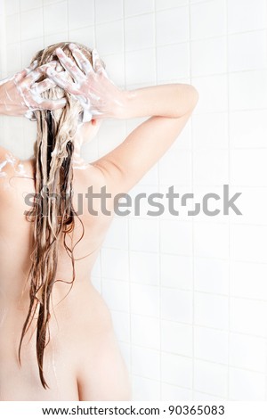 Beautiful nude young woman taking a shower and washing her very long blond hair, rear view on white background