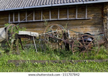 Retro old rusty farm tools of the early twentieth century rot near wooden house