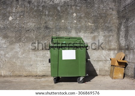 The lonely forgotten green trash bin in captivity of concrete walls