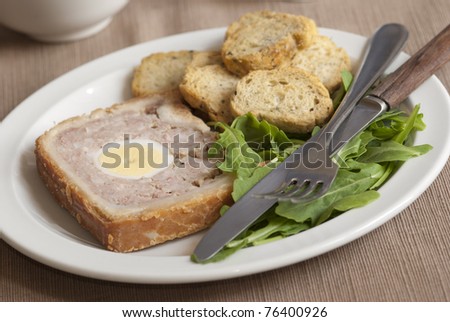 Freshly baked meat loaf with egg in the middle and rocket on a plate