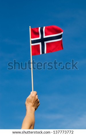 Norway flag in hand against blue sky.