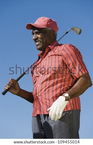 Happy senior African American man holding golf club against blue sky