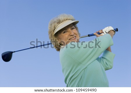 Portrait of a happy senior woman swinging a golf club against clear sky