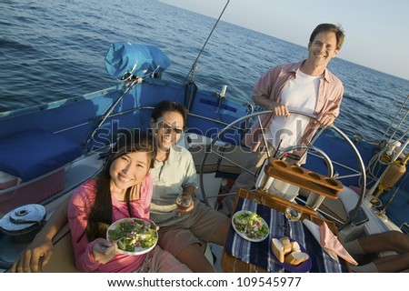 Happy couple having food with friend standing by the steering wheel of the yacht
