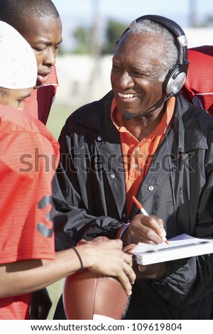Senior African American coach with football players noting down score in book