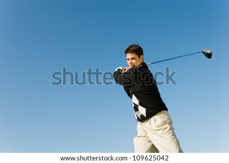 Young man swinging golf club against clear sky