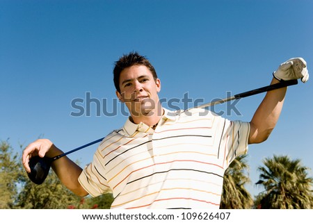Portrait of a confident young man with golf club against clear sky