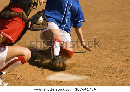 Female softball player sliding into base with baseman in the foreground