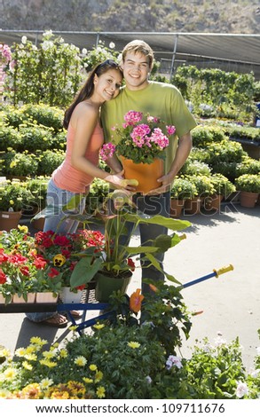 Portrait of a happy loving couple holding potted plant at botanical garden