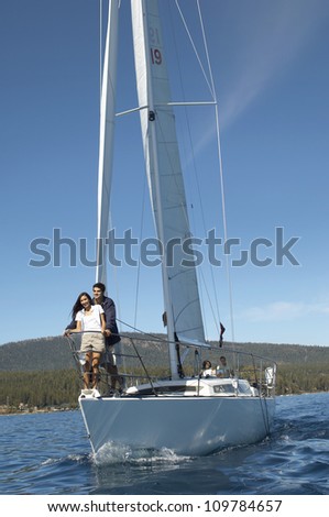 Middle aged couple standing on a sailboat with friends in background