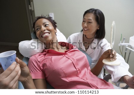 Happy female patient holding disposable cup while dentist looking at her