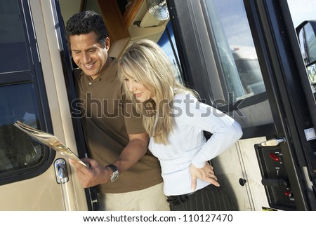 Happy couple at the entrance door of RV reading brochure