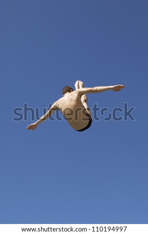 Diver diving in midair with arms out against clear sky