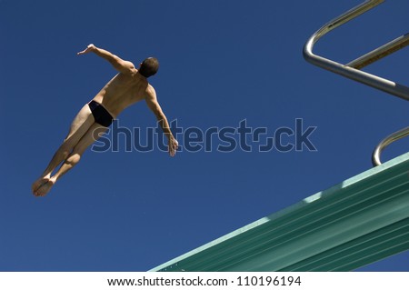 Low angle view of a male diver diving from springboard against the blue sky