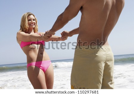 Happy young woman with man holding hands on beach